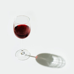 One glass of red wine on light background with hard shadow