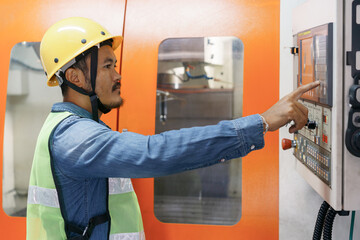Asian man engineer working on machine control panel display in factory
