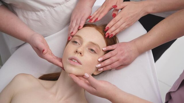 Close-up isolated photo of the face of a young woman who is surrounded by the hands of cosmetologists.