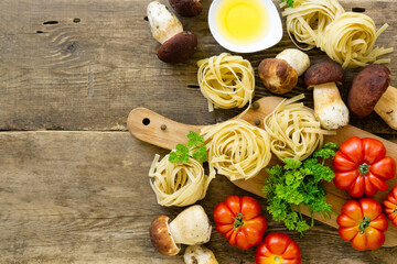 Ingredients for cooking pasta. Fettuccine with porcini mushrooms, tomatoes and greens on old wooden background