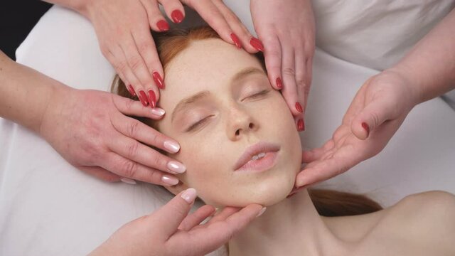 Close-up image of the face of a young woman who is surrounded by the hands of cosmetologists.