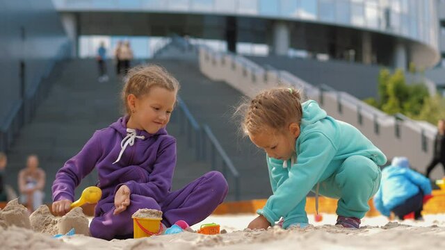 Two children 4-5 years old sitting in sandbox, playing with toys and buckets