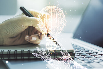 Creative light bulb illustration with hand writing in notepad on background with laptop, future technology concept. Multiexposure