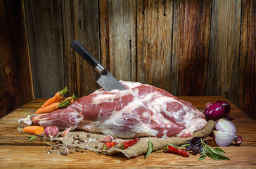 On a wooden table lies a raw leg of mutton on the bone pierced with a kitchen knife . Sheep meat with spices, close-up.A fresh piece of mutton. Horizontal view.Rustic style.