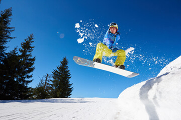 Snowboarding closeup in jump on blue sky background. Portrait of young man snowboarding in winter....