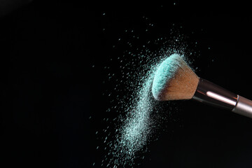 Makeup brush and burst of cosmetics on dark background