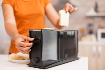 Woman waiting for roasted bread to pop from electric toaster. Housewife using bread toaster for delicious breakfast. Healthy morning in cozy interior, delicious home meal preparation