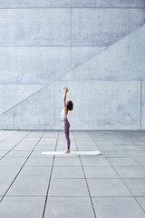 Frau/Mädchen in Pastell gekleidet macht Outdoor Yoga Übungen/Sonnegruß in moderner Beton...