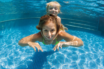 Happy family - young mother, baby boy learn to swim, dive underwater. Jump with fun in swimming pool. Healthy lifestyle, active parents, people water sports activities on summer holidays with kids.