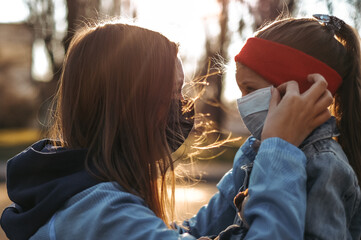 The mother puts a surgical mask on the baby's face. A little girl goes to school during the quarantine period. The concept of the coronavirus COVID-19.