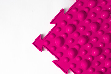 Pink orthopedic mat in the form of small stones on a white background for foot massage. Prevention of children's flat feet