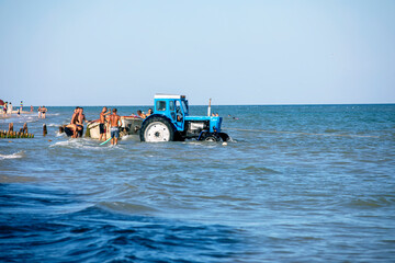 blue tractor tows a boat into the open sea on the beach. horizontal format