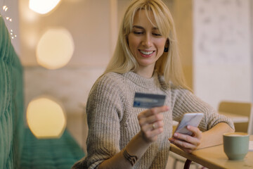 Portrait of attractive blonde woman using a credit card to make an online payment at cafe.