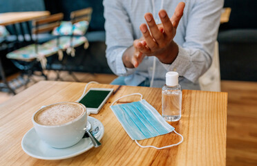 Unrecognizable man disinfecting his hands with hydroalcoholic gel in a coffee shop