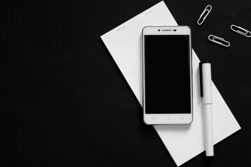 Creative flat lay, black and white photo of workspace desk with smartphone, notepad, pen and some paper clips with a copy space background, minimal styled, elective focus