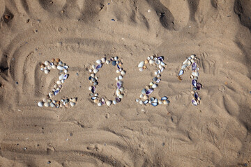 Fototapeta na wymiar The numbers 2021 are written and lined with seashells in the sand. New year on the beach. Sea coast. Place for your text. Summer in winter. Natural background.