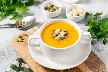 Pumpkin soup. Pumpkin cream soup in a white plate on the light gray kitchen table. Vegetarian...