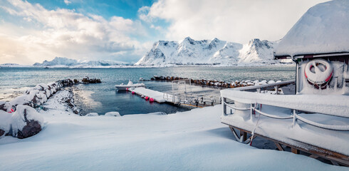 Snowy morning view of Vestvagoy island with small pier, boat and wooden dock. Panoramic winter scene of Lofoten islands, Norway, Europe. Stunning seascape of Norwegian sea.  Life over polar circle..