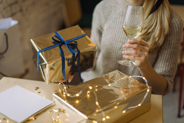 Cropped shot of stylish young woman holding a glass of white wine and Christmas or birthday present. Concept of romantic celebration dinner with gifts exchanging.