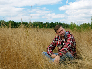 Naklejka na ściany i meble A man in a red shirt relaxes and rests in nature sitting in the grass field.