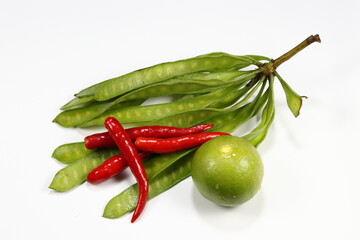 Pile of traditional ingredients in Thai local cuisine, bunch of acacia, fresh red chilly and lime isolated on the white background. Famous tropical vegetable concept. 