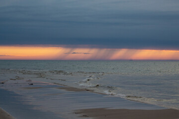 Piękny zachód słońca nad morzem. Na horyzoncie widać jak pada deszcz. © Anastasiia