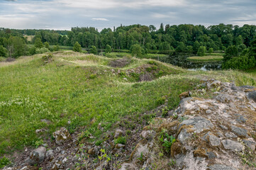 Fototapeta na wymiar Castle ruins abandoned in the infinite beauty of the expansive green with river view. Rūjiena castle ruins.