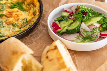 Omelet in a frying pan with parsley and dill. Serve with fresh bread and fresh vegetables.