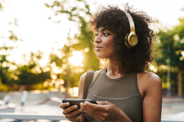Image of african american sportswoman using cellphone and headphones