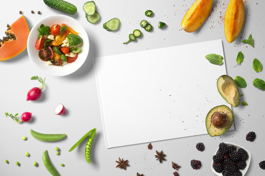 Top view kitchen counter with avo, papaya, radishes, berries, mango and a bowl of salad with a blank piece of paper