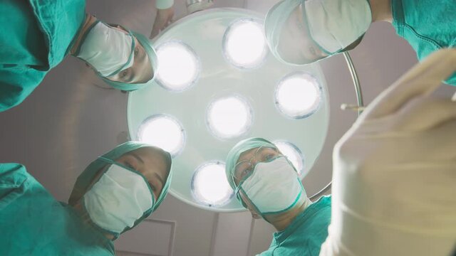 Bottom up view : Group of asian doctor, nurse and staff in surgeons holding medical instruments in hands, looking at patient and operating. Teamwork, Healthcare and medicare concept.