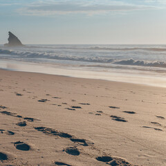 tourist footprints are visible on the hot summer sand of the ocean beach near the Portuguese city of Sintra