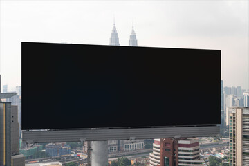 Blank black road billboard with Kuala Lumpur cityscape background at day time. Street advertising poster, mock up, 3D rendering. Front view. Concept of marketing to promote or sell services or ideas.