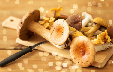 cooking, culinary and edible mushrooms concept - different edible mushrooms and kitchen knife on...