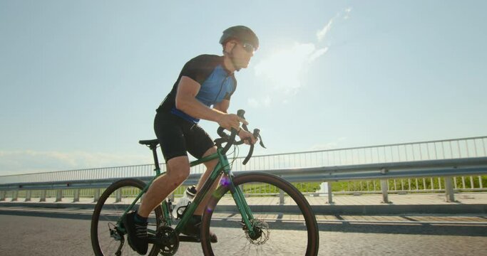 A sportsman on a bicycle is standing on the pedals and developing great speed. Training on a bicycle. Sun in the background. 4K