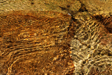 Water ripples in a stream flowing over orange-brown rock abstract texture background