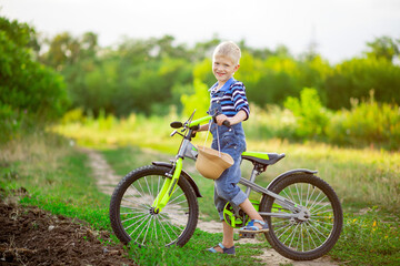 happy baby boy blond with a Bicycle stands in a field in summer, children's lifestyle