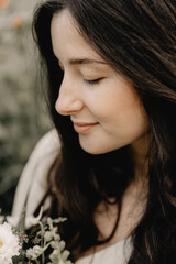 portrait of a pretty young girl dressed in a long linen dress posing for a photo among flowers at a...