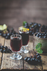homemade black chokeberry wine or liqueur with ripe berries on wooden background