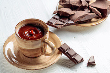 Hot chocolate and broken pieces of bitter chocolate on a white wooden table.