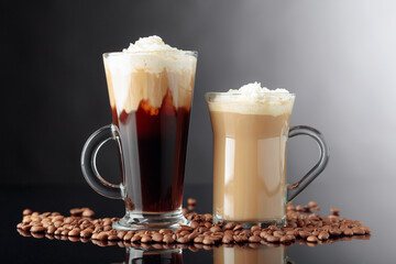 Irish coffee and latte on a black reflective background.