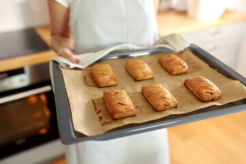food cooking, culinary and people concept - young woman with towel holding hot baking tray with jam pies at home kitchen