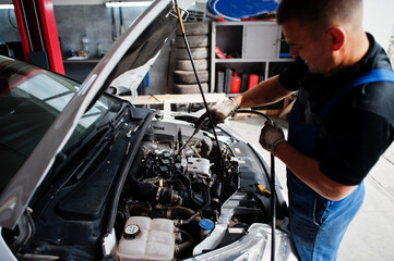 Car repair and maintenance theme. Mechanic in uniform working in auto service, checking engine.