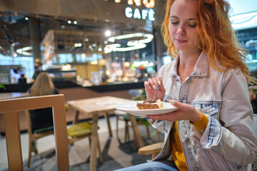 Young red haired woman eating dessert at shopping mall