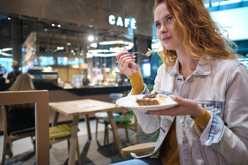 Young red haired woman eating dessert at shopping mall