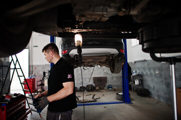 Fototapeta na wymiar Car repair and maintenance theme. Mechanic in uniform working in auto service.