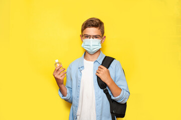 A schoolboy boy in a medical mask with an antibacterial sanitizer in his hands on a blue background. Education during the epidemic.
