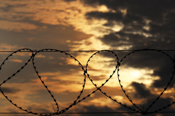 Barbed wire on dramatic sky background at sunset. Concept of boundary, prison, war or immigration