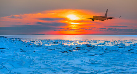 Airplane in the sky at sunset - Beautiful landscape cracking ice, frozen sea coast at sunrise 