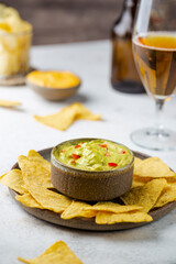 Nachos chips in a bowl with sauces guacamole and beer over white stone background.